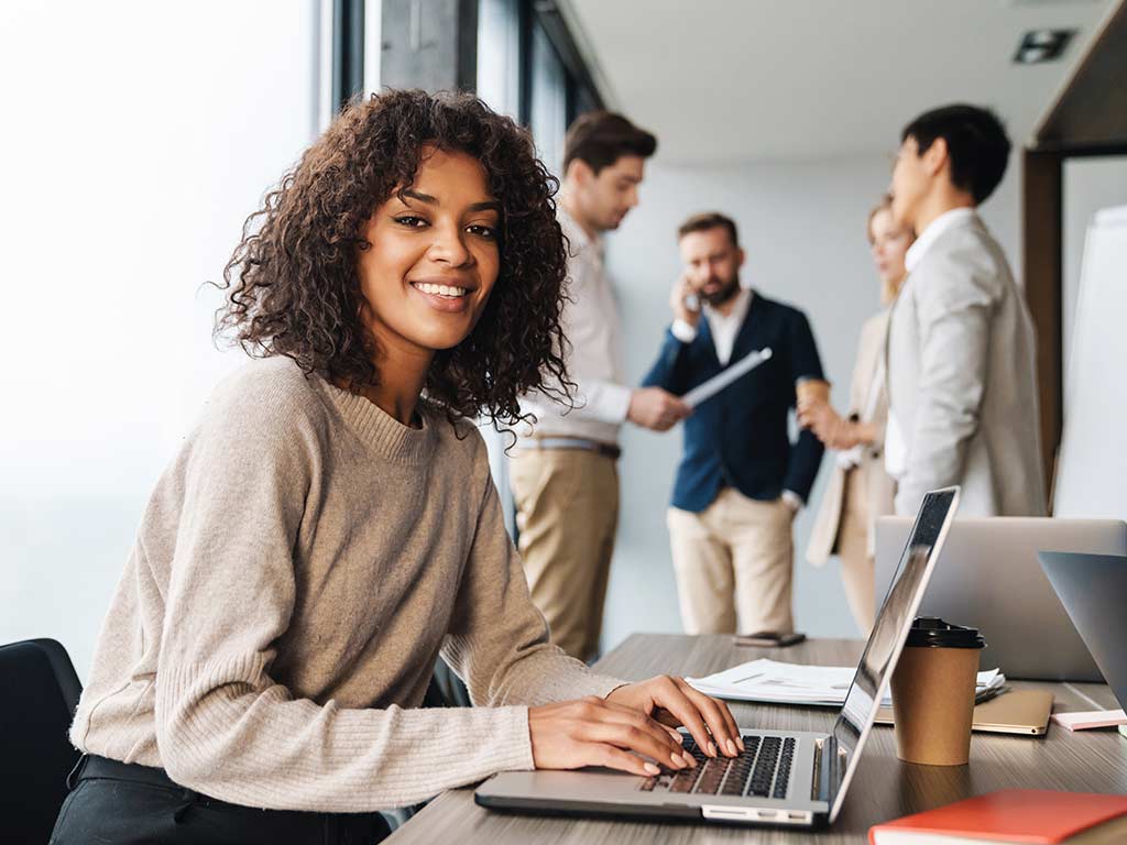 Professional young woman smiling towards the camera while working on her laptop